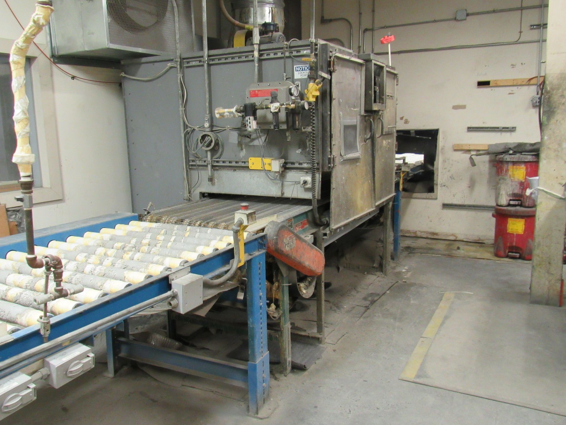 Industrial oven with roller conveyor belt in a factory setting.