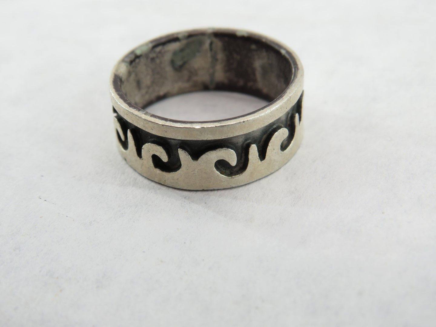 Silver ring with a wavy, decorative pattern around the band.