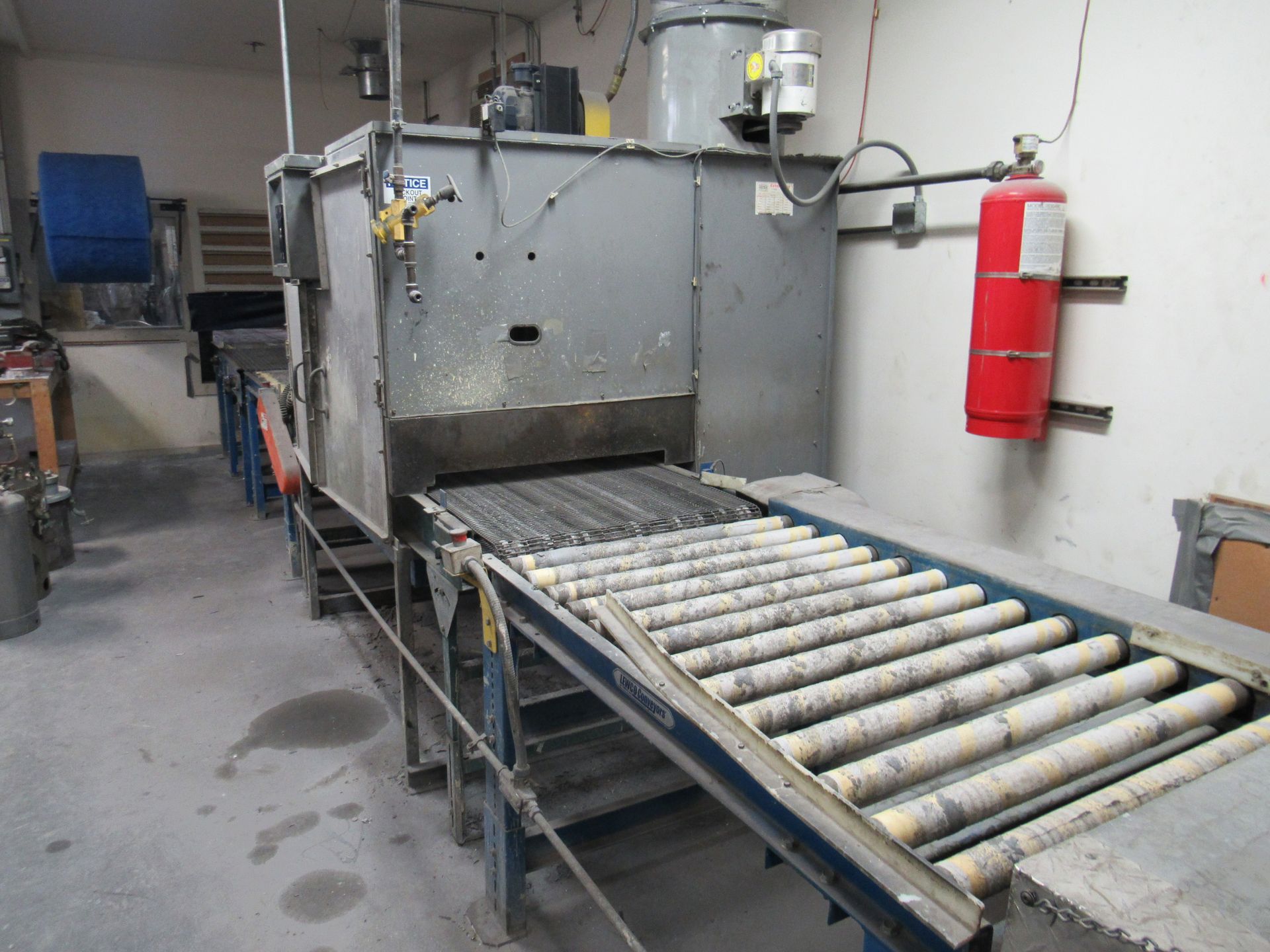 Industrial oven with a roller conveyor belt. Grey metal with a red fire extinguisher on the side.