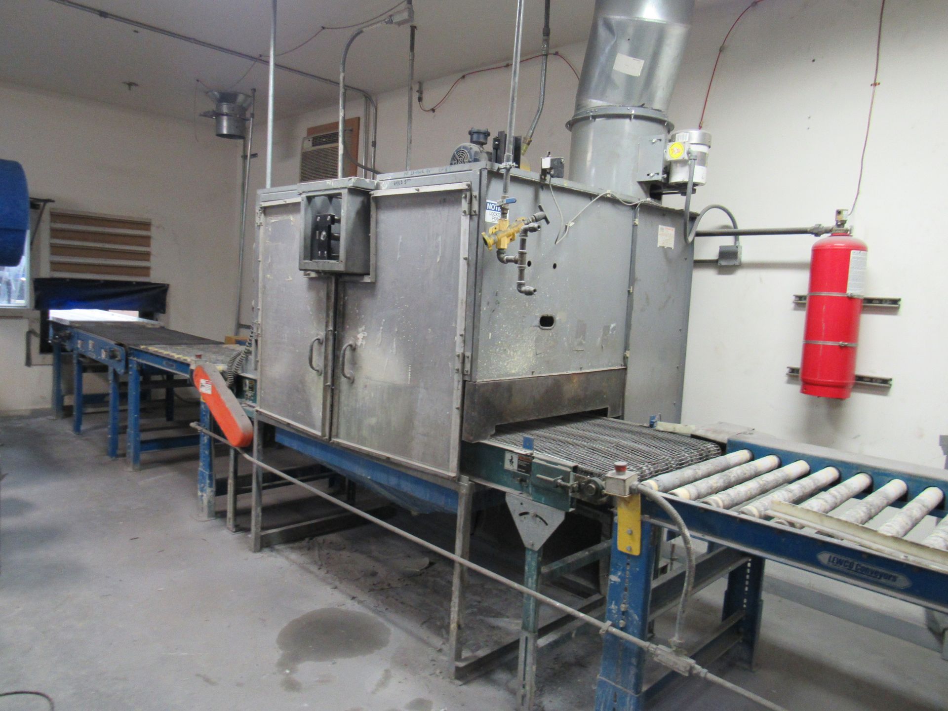 Industrial oven on a conveyor belt system in a factory setting, with attached exhaust.