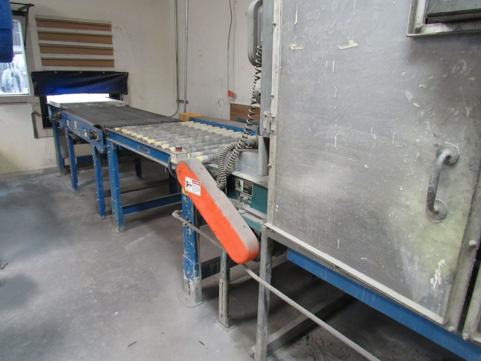 A conveyor belt system with an orange motor, leading into an industrial oven in a factory setting.