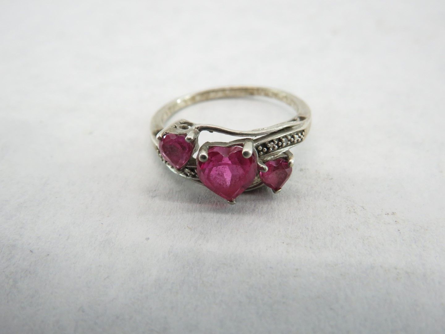 Silver ring with three heart-shaped, pink gemstones and small accent stones.
