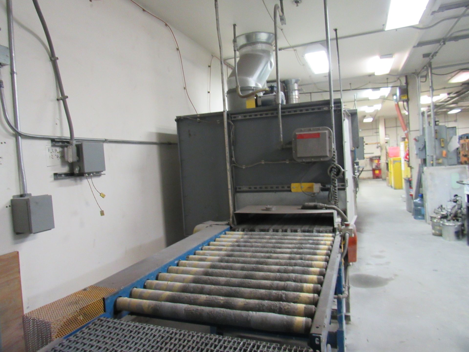 Industrial shot blasting machine with rollers in a factory setting.