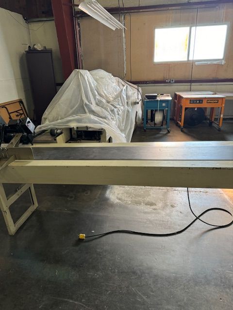 A large, covered industrial machine with a long table in a warehouse setting.