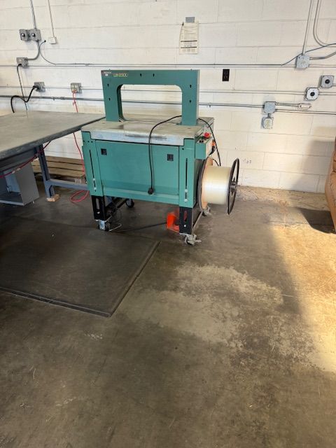 Green industrial strapping machine with a roll of strapping in a warehouse setting.