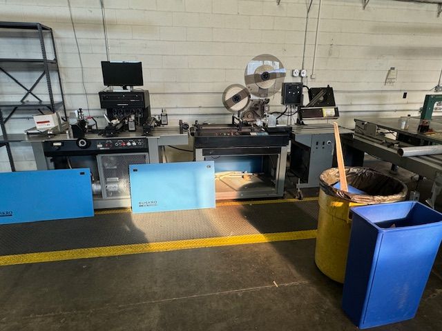 Industrial machines in a workshop with various equipment and bins, a yellow line on the floor.