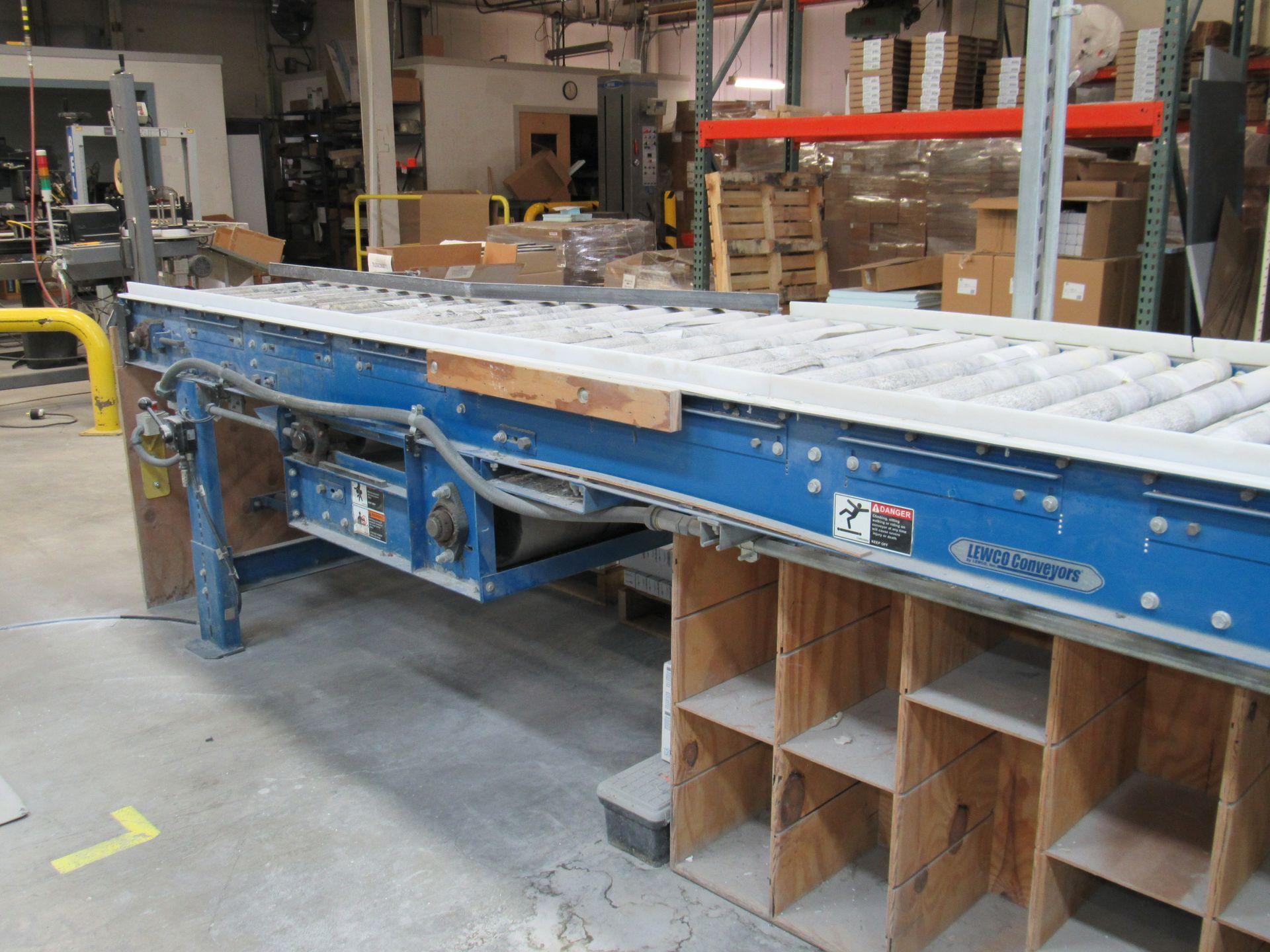 Blue industrial conveyor belt over wooden shelving in a warehouse.