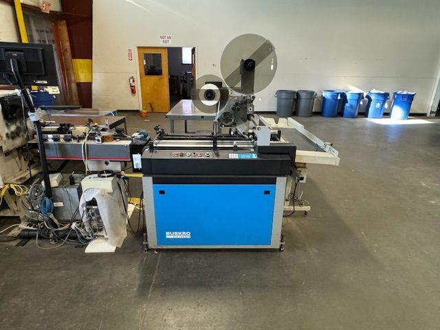 Blue and gray industrial labeling machine in a warehouse setting.