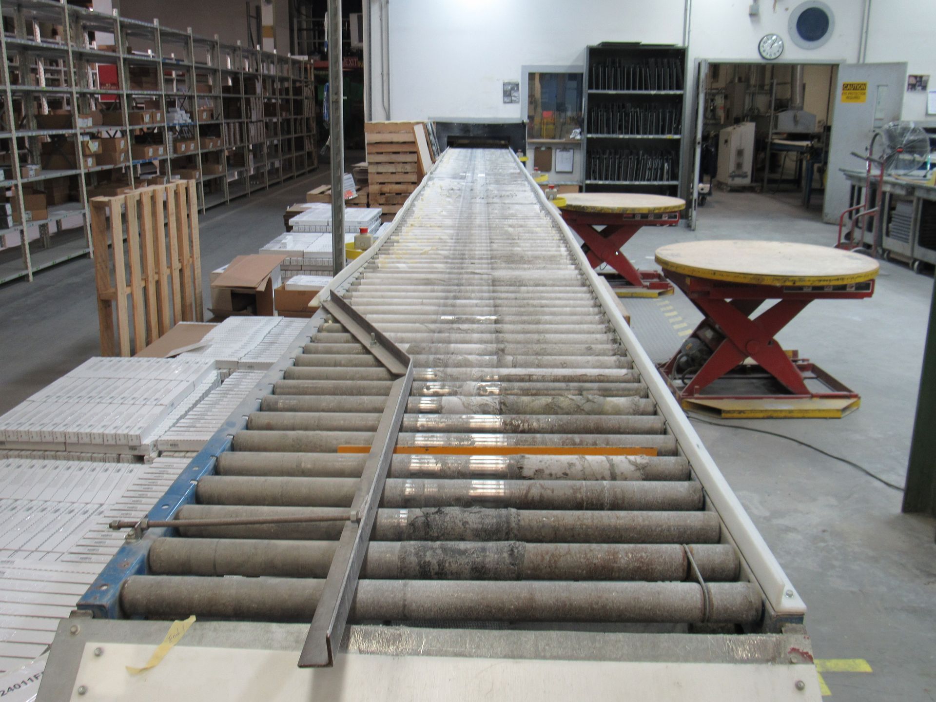 Warehouse conveyor belt with rollers, extending from a pallet of tiles toward the back of the building.