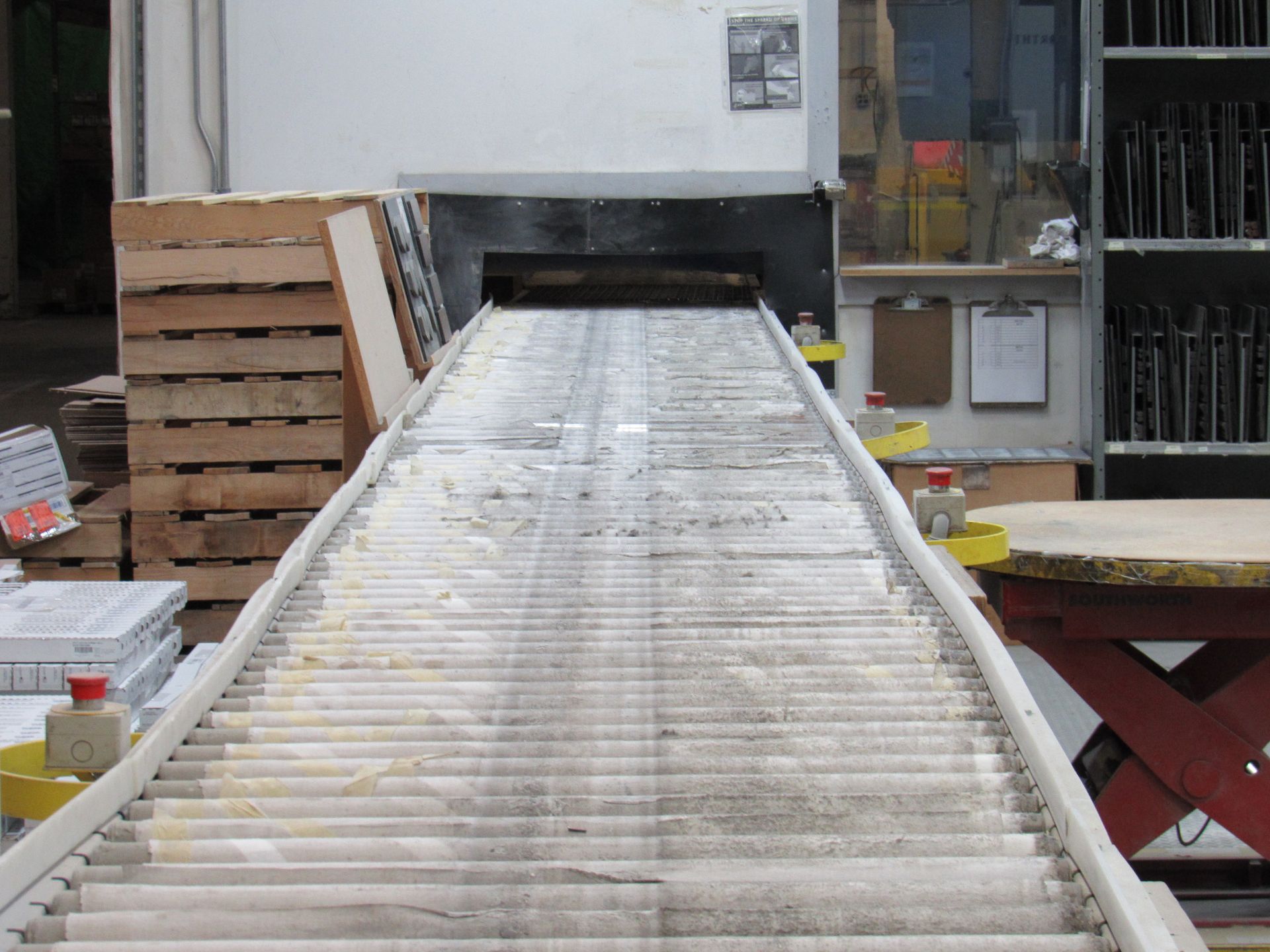 Conveyor belt leading into a dark tunnel. Industrial setting with pallets and shelves.