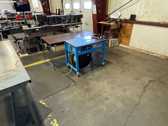 Blue work table on wheels in a workshop with cables and a large spool.
