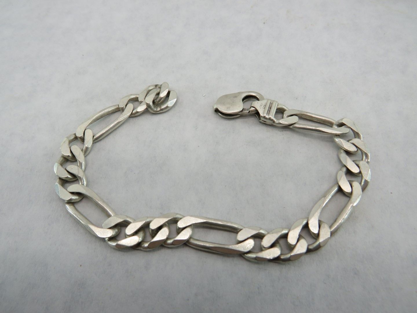Silver Figaro chain bracelet, clasp open on a gray background.