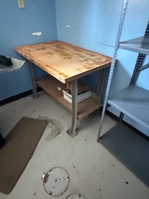 Work table with a wooden top and metal legs in a blue-walled room with metal shelving.
