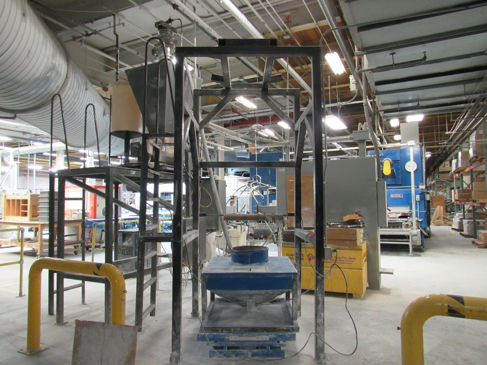 Industrial machinery in a factory setting, with metal frames, tanks, and a blue machine.