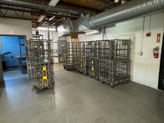 A warehouse interior with multiple metal rolling carts stacked near a wall, and an open doorway on the left.
