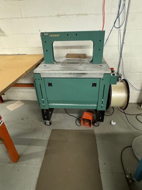 Green strapping machine with a spool of strapping material in a workshop.