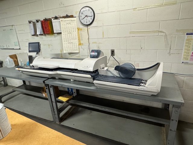 Long mailing machine on a metal table in an industrial setting.
