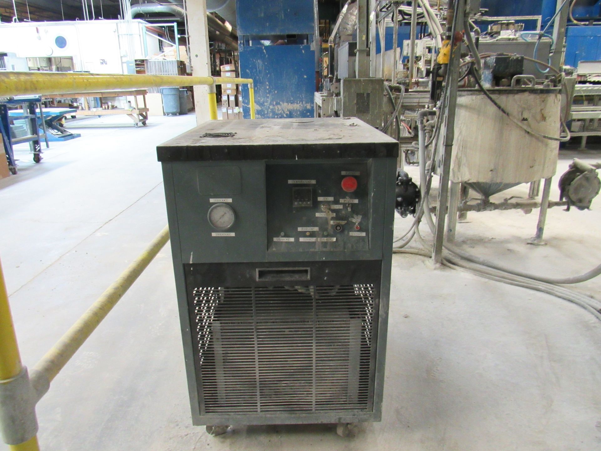 Industrial chiller with control panel and air vents, on wheels in a factory setting.