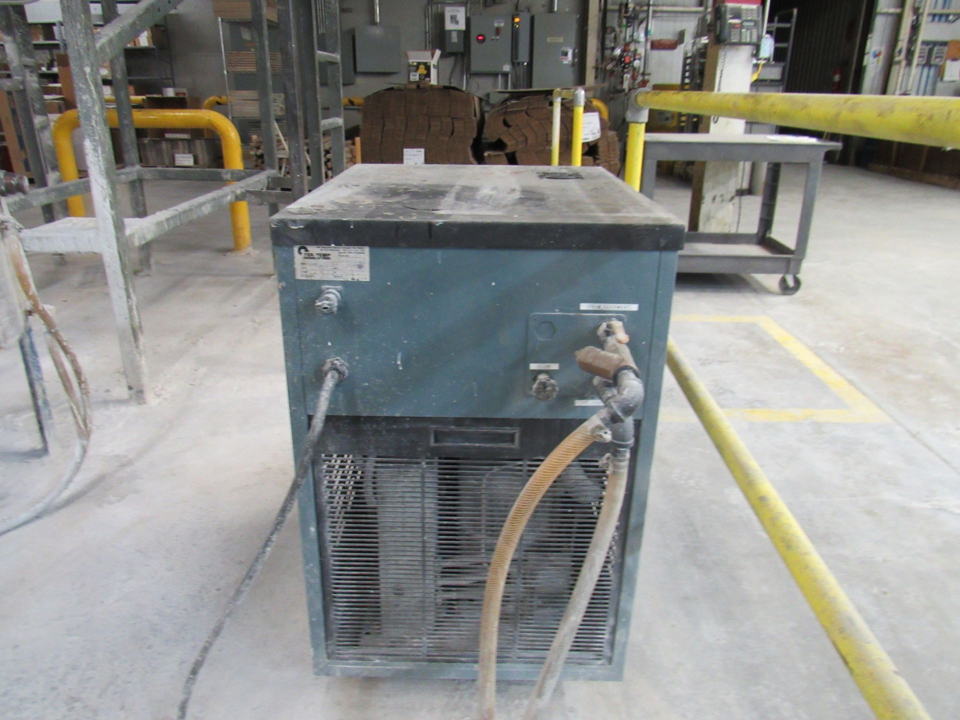 Blue industrial chiller in a factory setting, with visible hoses and vents.
