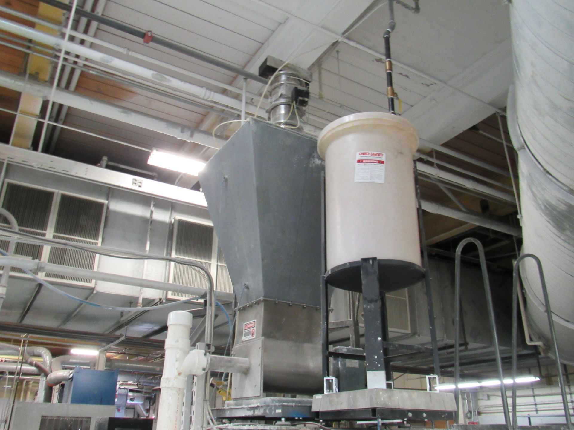 Industrial machinery with a large gray hopper and a white cylindrical container.