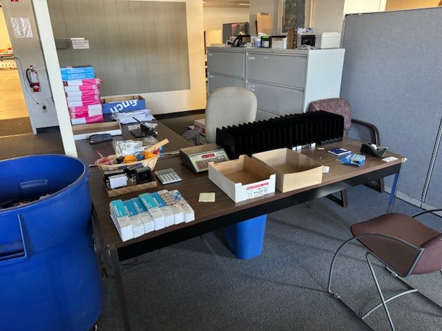 Office desk with various items: boxes, scales, and a blue trash bin.