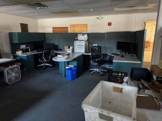 An office with desks, cubicles, office chairs, and clutter.