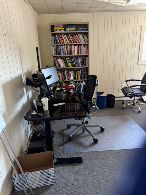 Office with desk, computer setup, bookshelf, and two office chairs on carpeted floor.