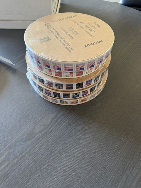 Three rolls of postage stamps stacked on a wooden surface.