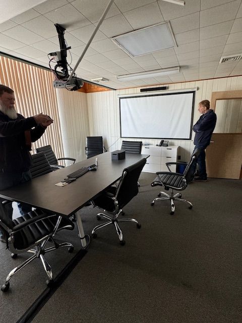 A conference room with a projector, screen, table, and chairs.
