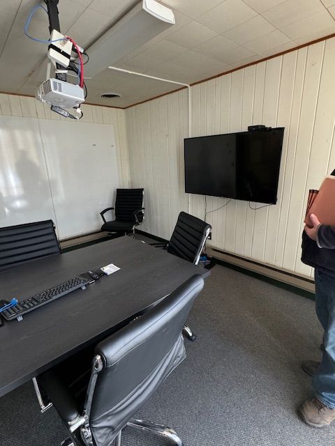 Conference room with a table, chairs, TV, whiteboard, and projector.