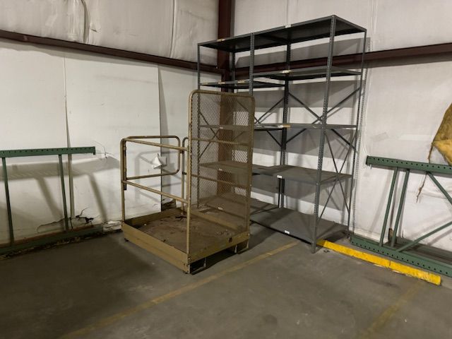 Warehouse interior with metal shelving units and a rolling platform with a railing.
