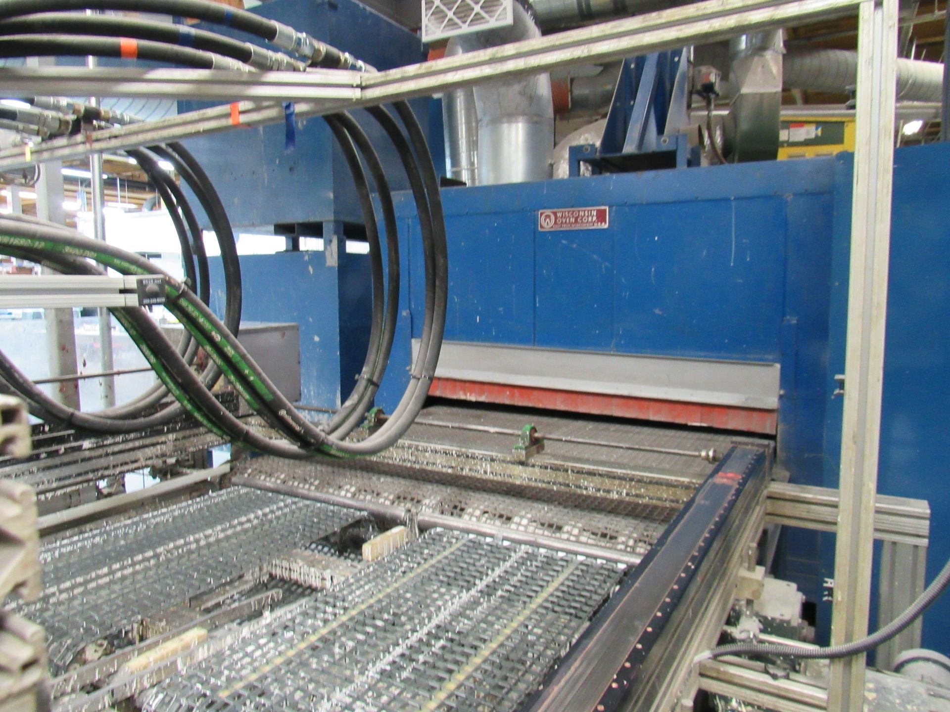 Blue industrial oven with black tubes and a metallic conveyor belt.