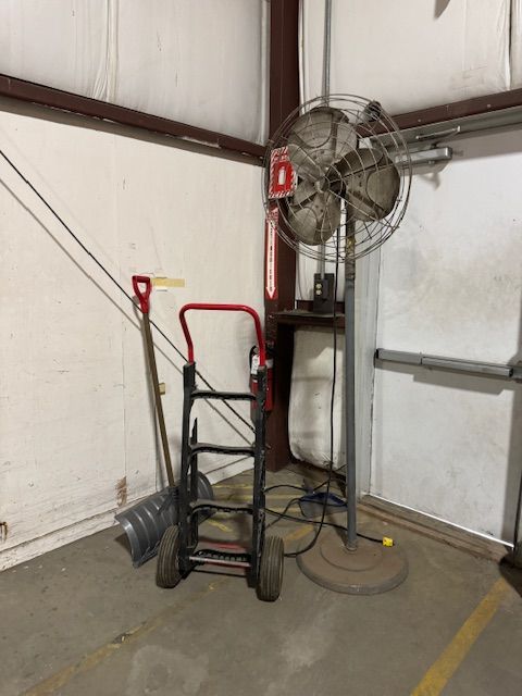 Industrial fan, hand truck, and shovel in a corner of a building.
