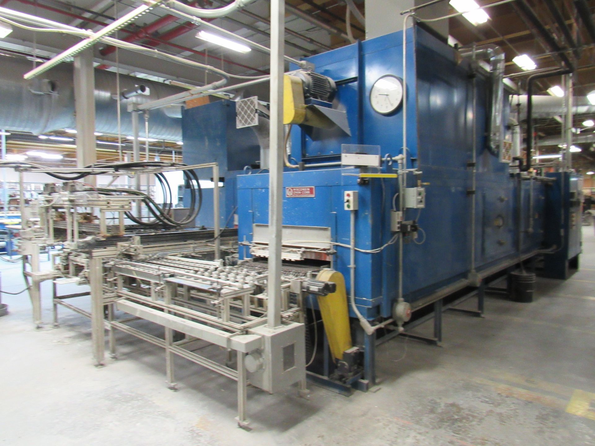 Blue industrial oven with conveyor system in a factory setting.