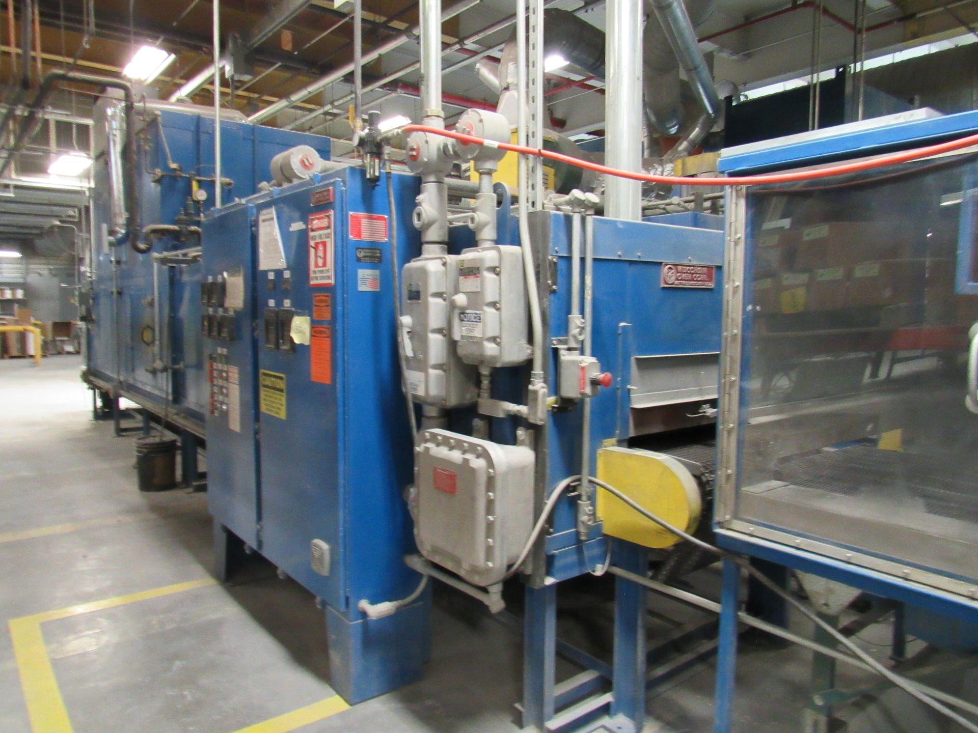 Blue industrial oven with control panel and conveyor belt in a factory setting.