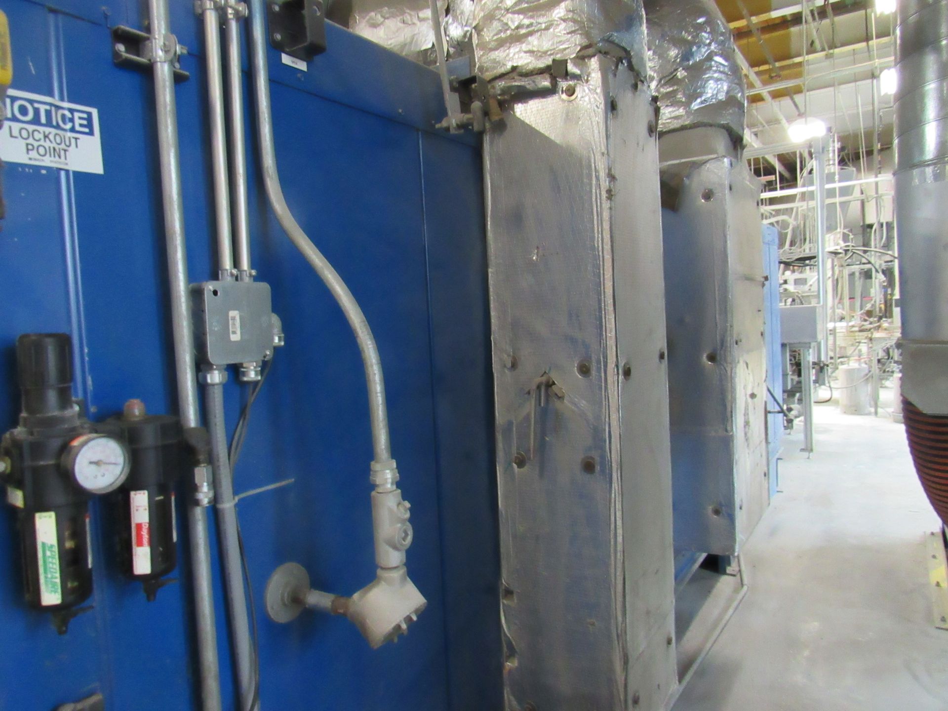 Blue industrial oven with pipes and gauges on a factory wall.