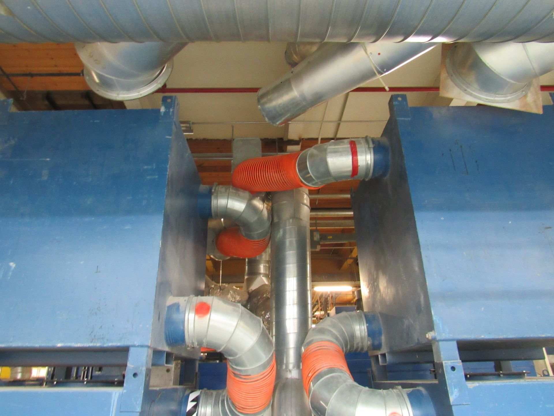 Blue machinery with gray and orange pipes, and ductwork overhead.