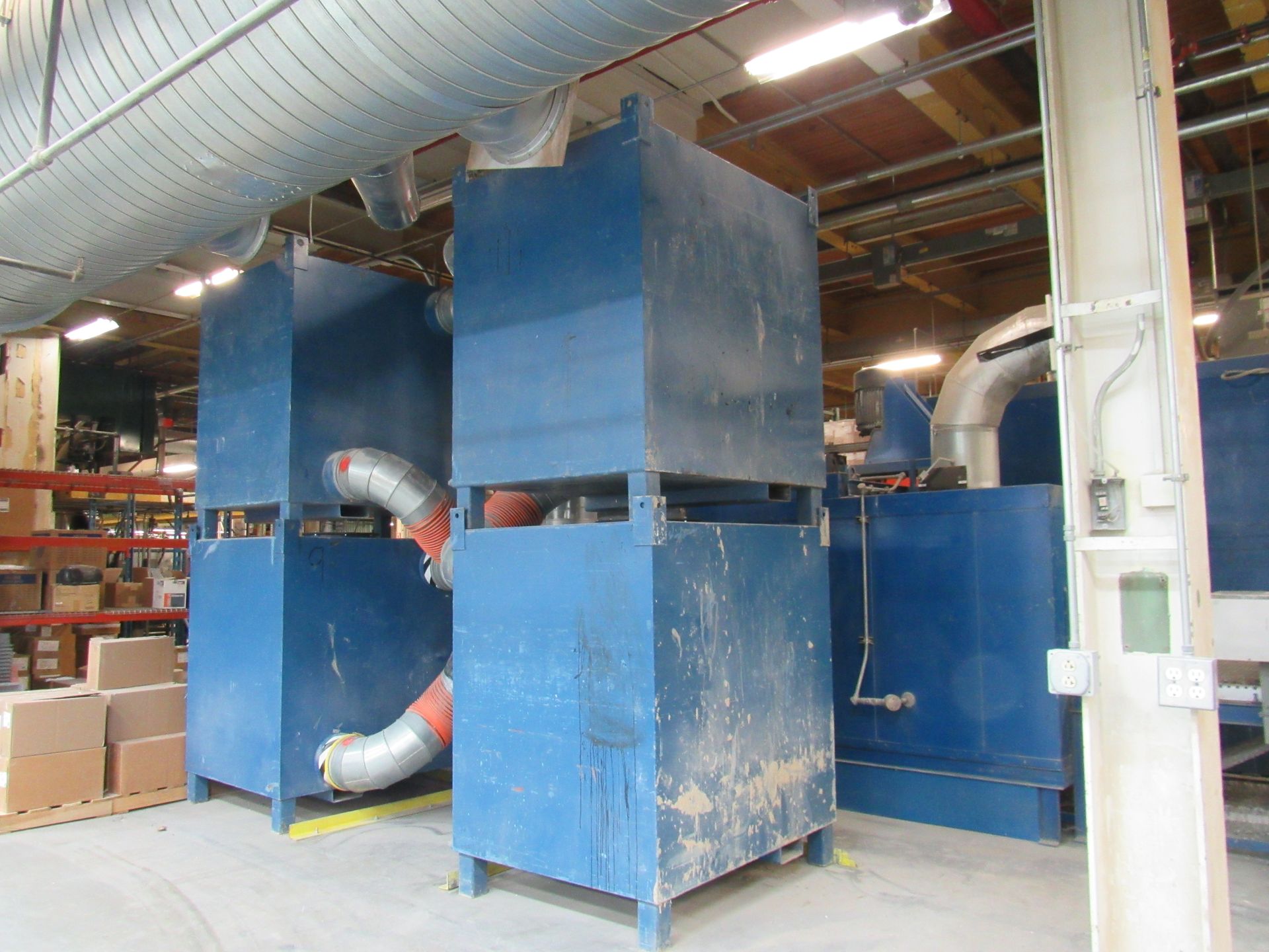 Blue industrial dust collection units in a factory setting, with ductwork.