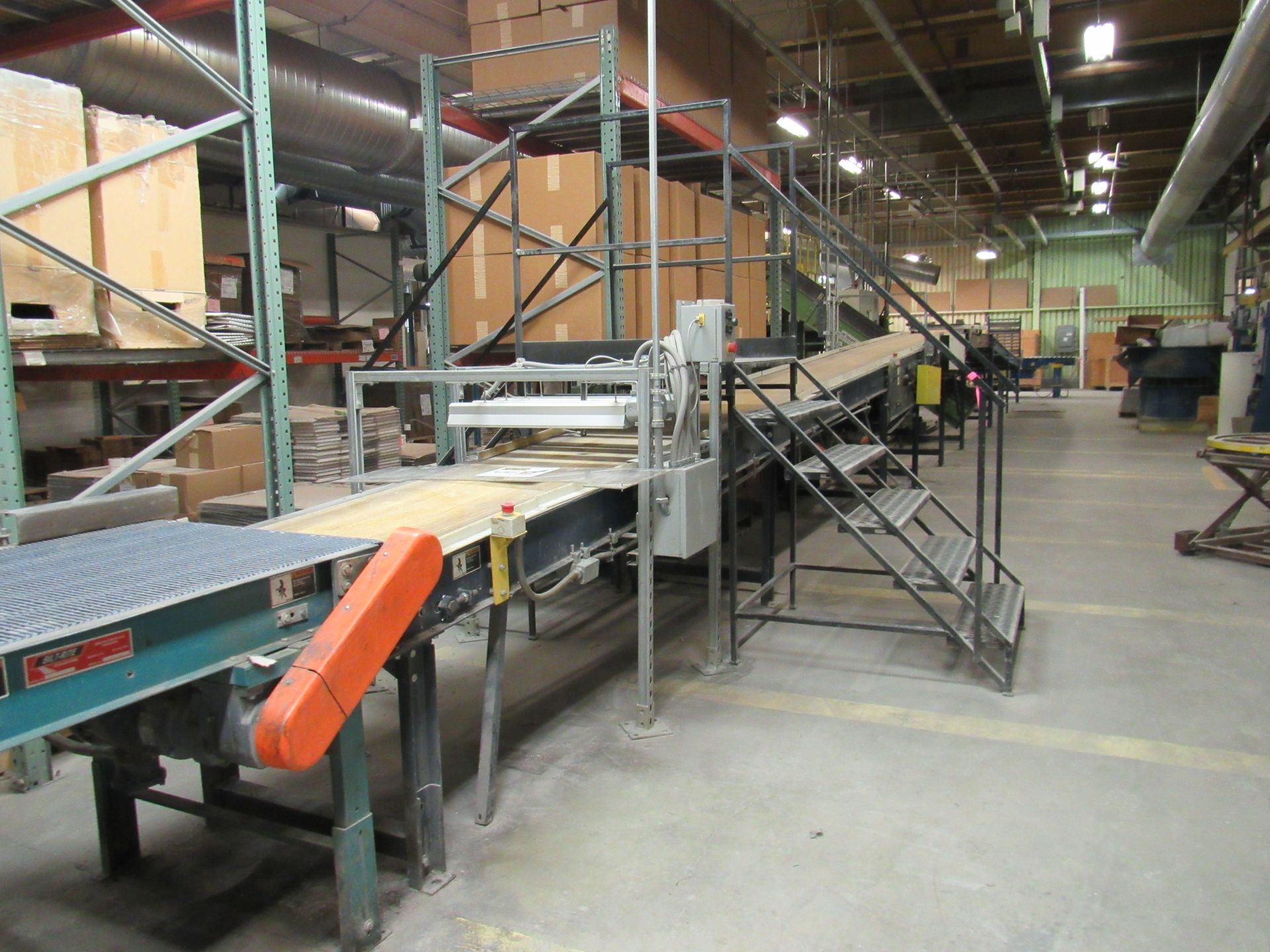 Conveyor belt system in a warehouse setting, with steps and shelving holding boxes.
