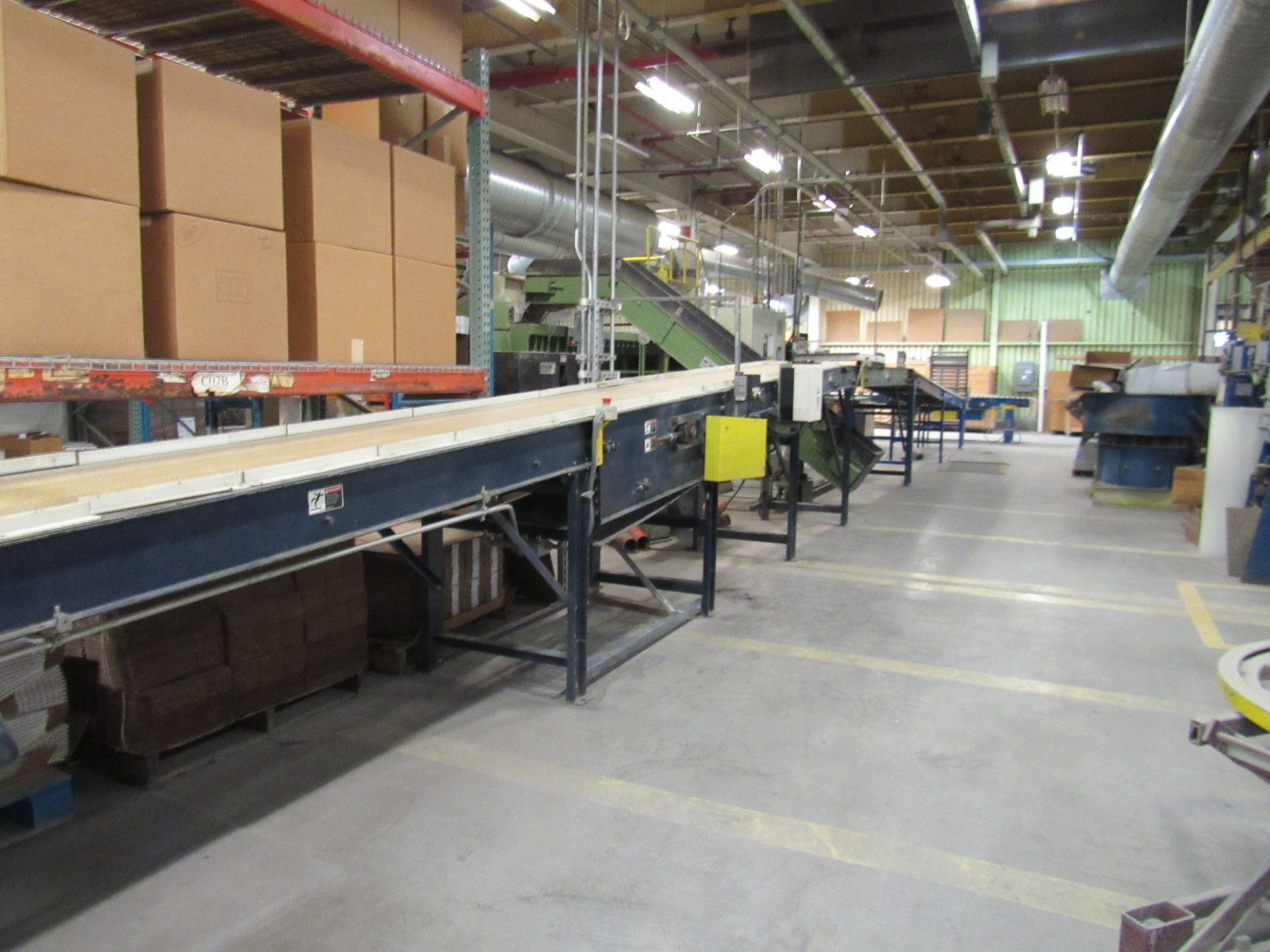 Conveyor belt system in a factory setting with cardboard boxes on shelves.
