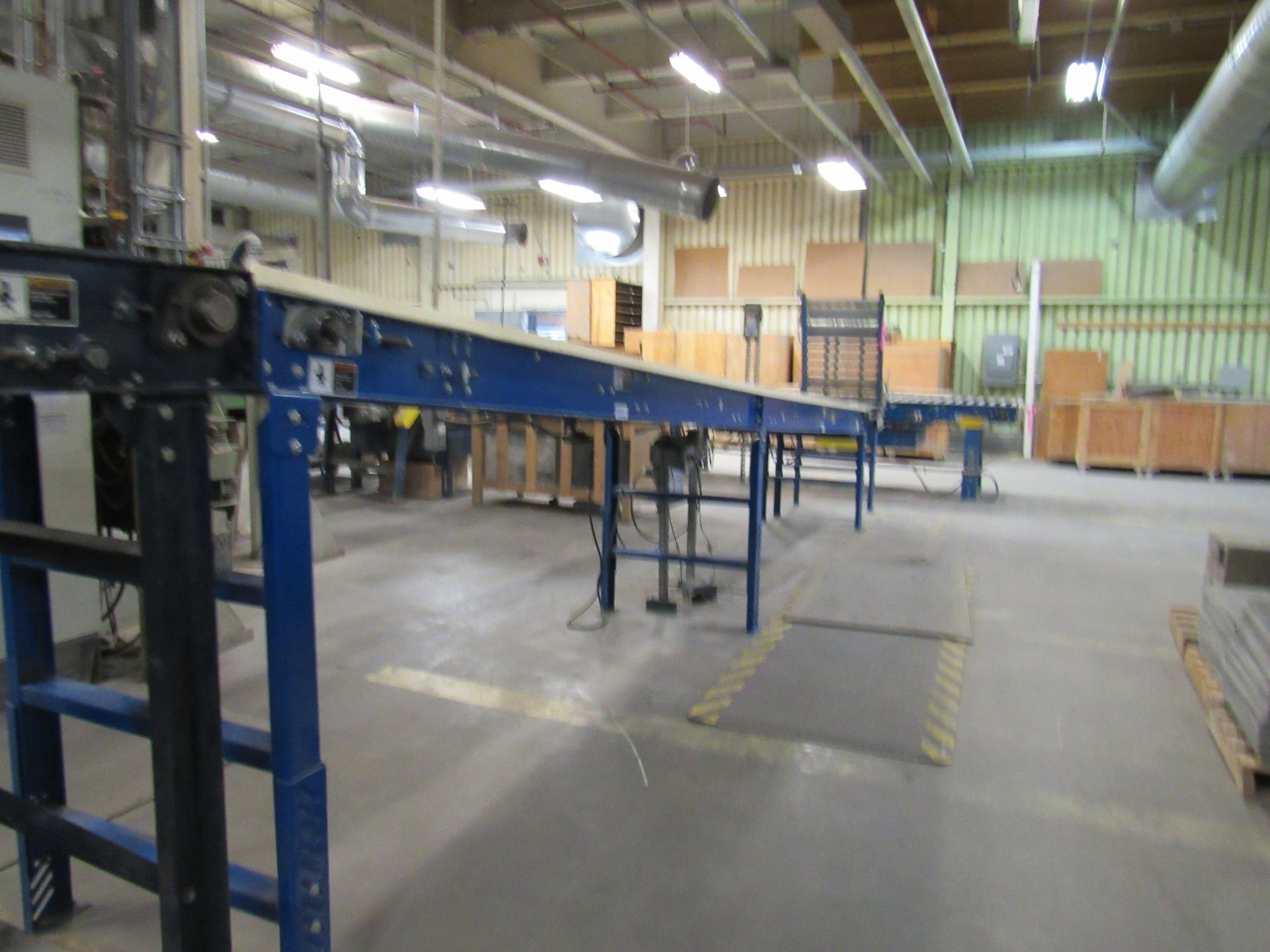 Blue conveyor belt in a factory setting, stretching toward the back, near a pallet of wooden boxes.