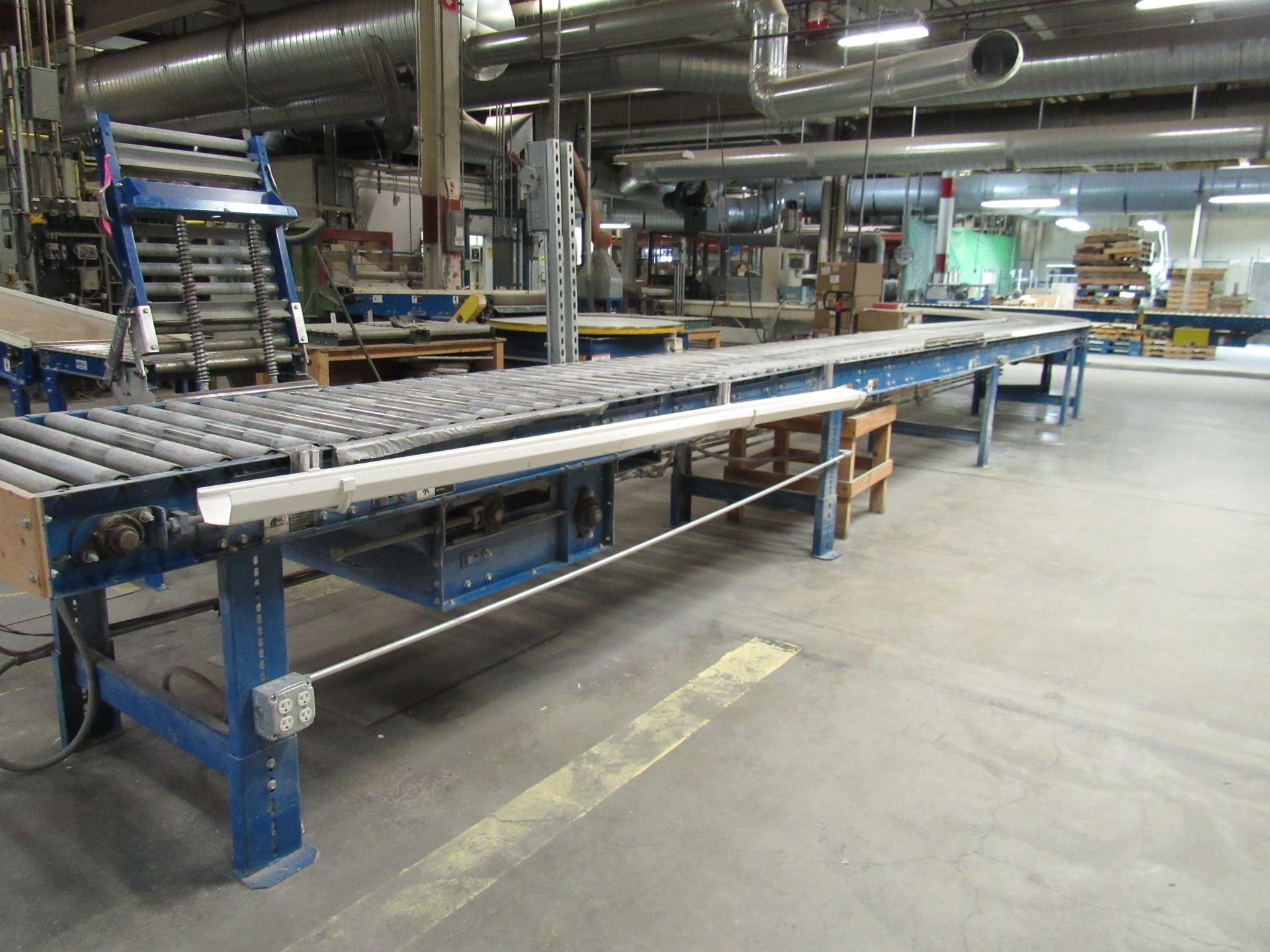 Roller conveyor belt in a factory setting, blue frame, gray rollers, and concrete floor.