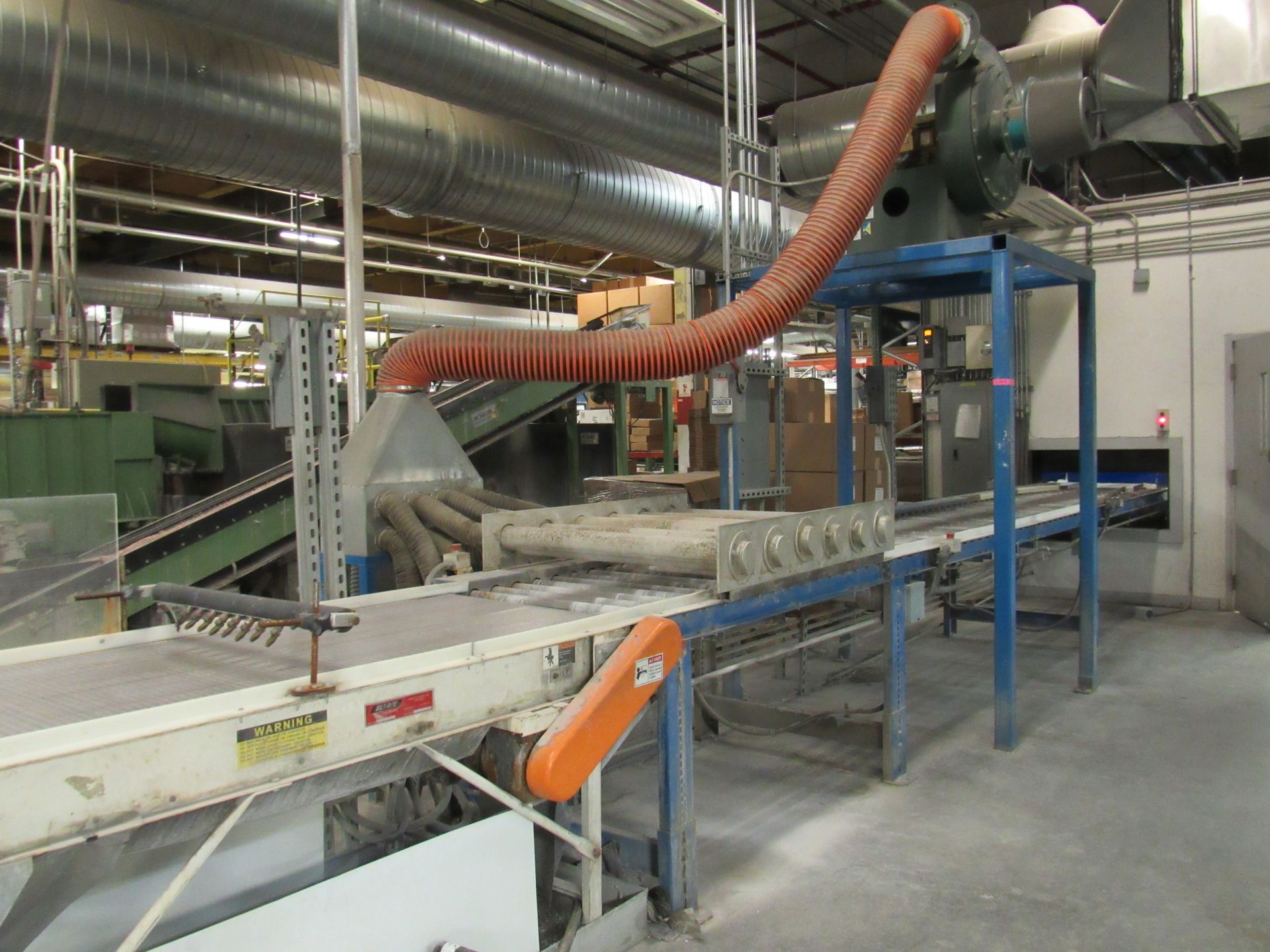 Conveyor belt in a factory. Orange hose overhead, blue metal frame, and air duct.