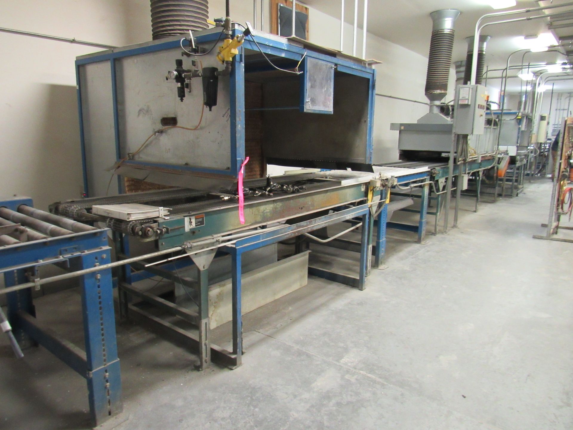 Industrial assembly line with blue metal frames and conveyor belts, in a gray-floored workshop.
