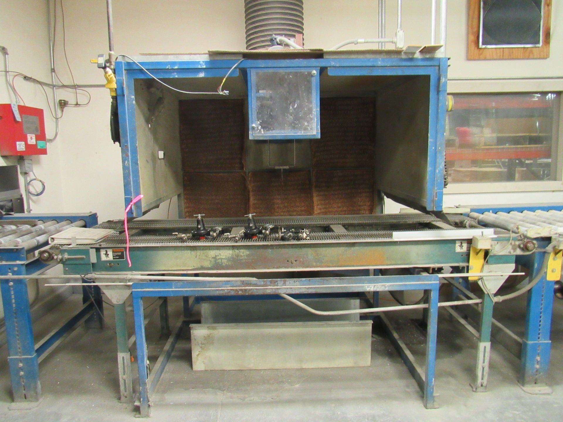 Spray booth in industrial setting with parts on a conveyor belt. Blue and gray structure.