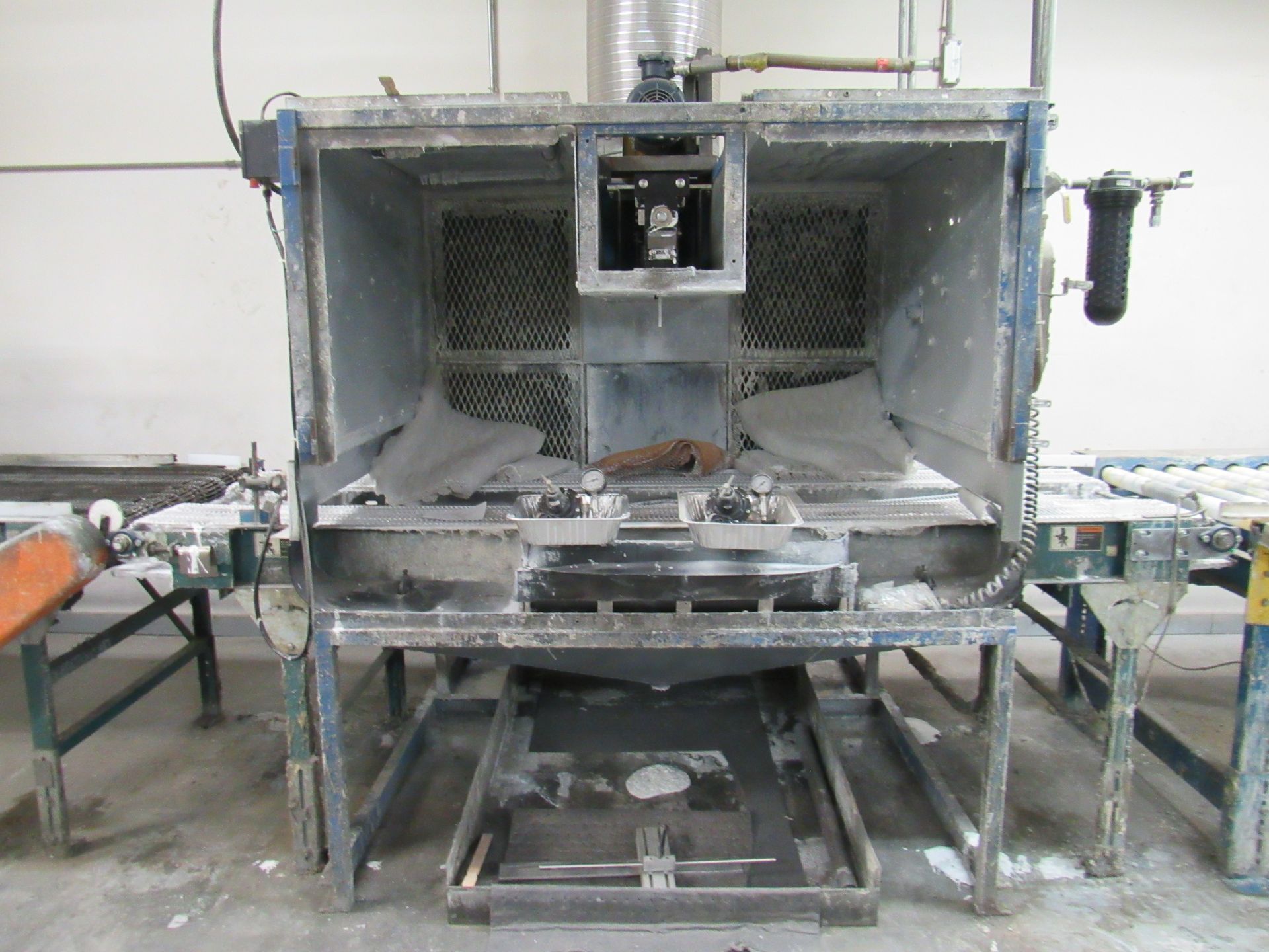 An industrial sandblasting cabinet with an open door, and a conveyor belt to the right.