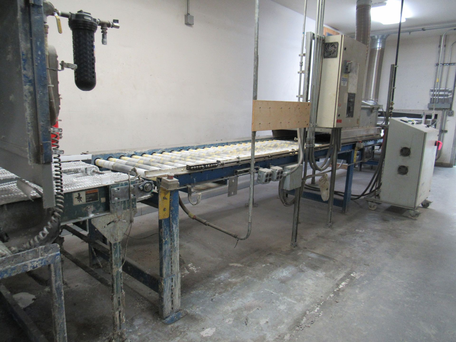 Conveyor belt in a factory with equipment and electrical panel visible.