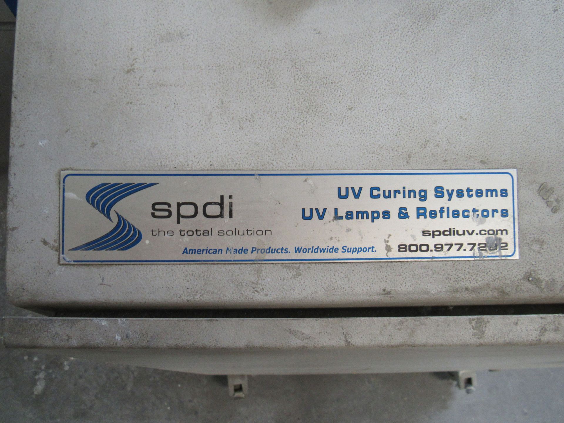 Close-up of a silver sign on a UV curing system, with the company name SPDI and contact information.