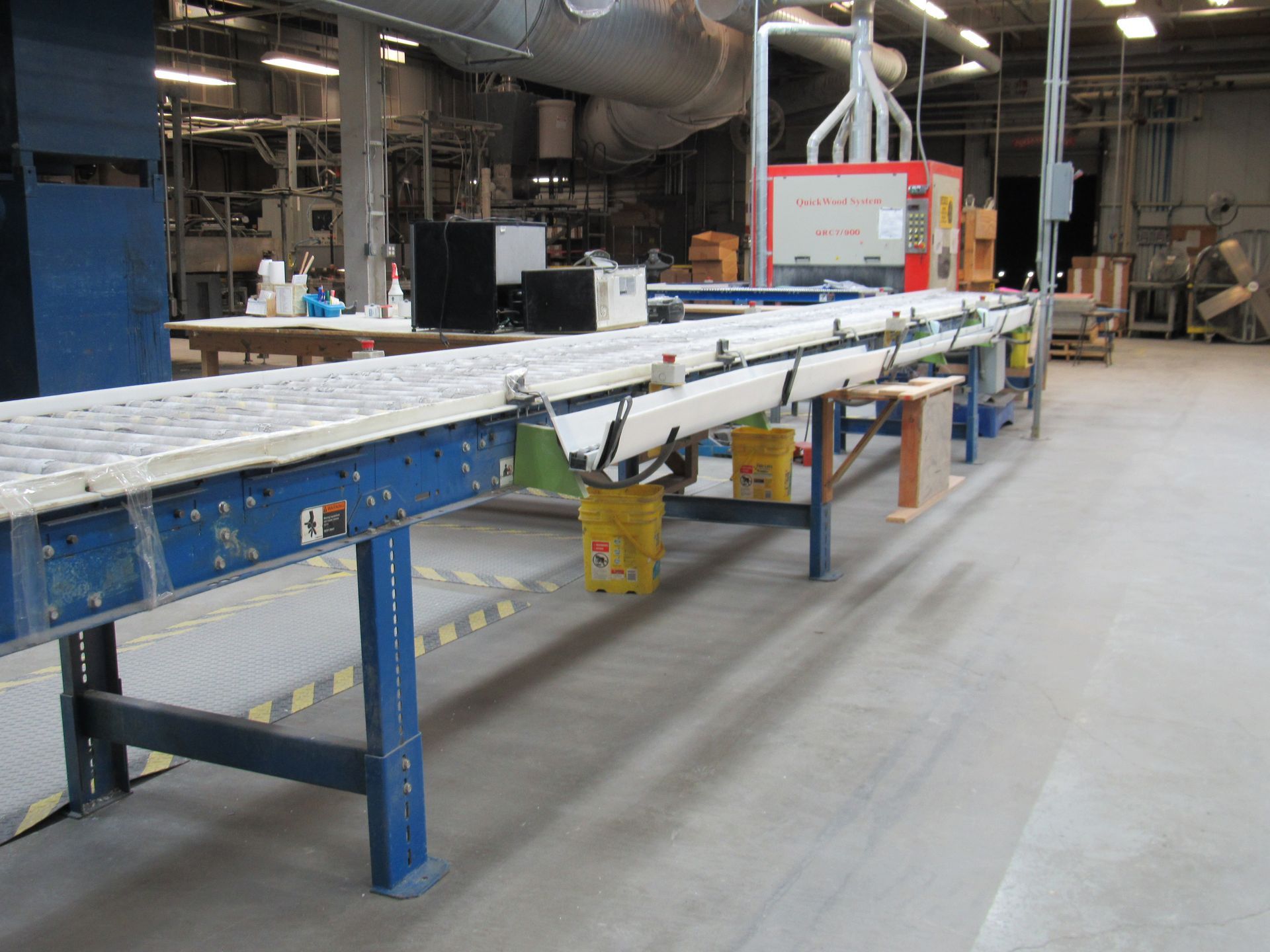 Conveyor belt in a factory setting. Yellow buckets hang below.