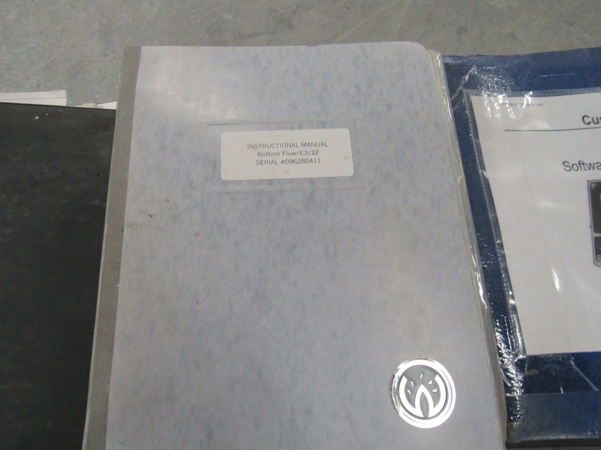 Notebook with a label and a silver logo next to a binder in plastic wrap.
